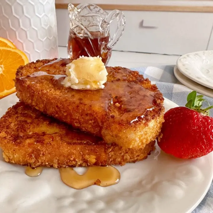 Two slices of Crispy Cinnamon Corn Flake French Toast stacked on top of each other with butter and maple syrup.
