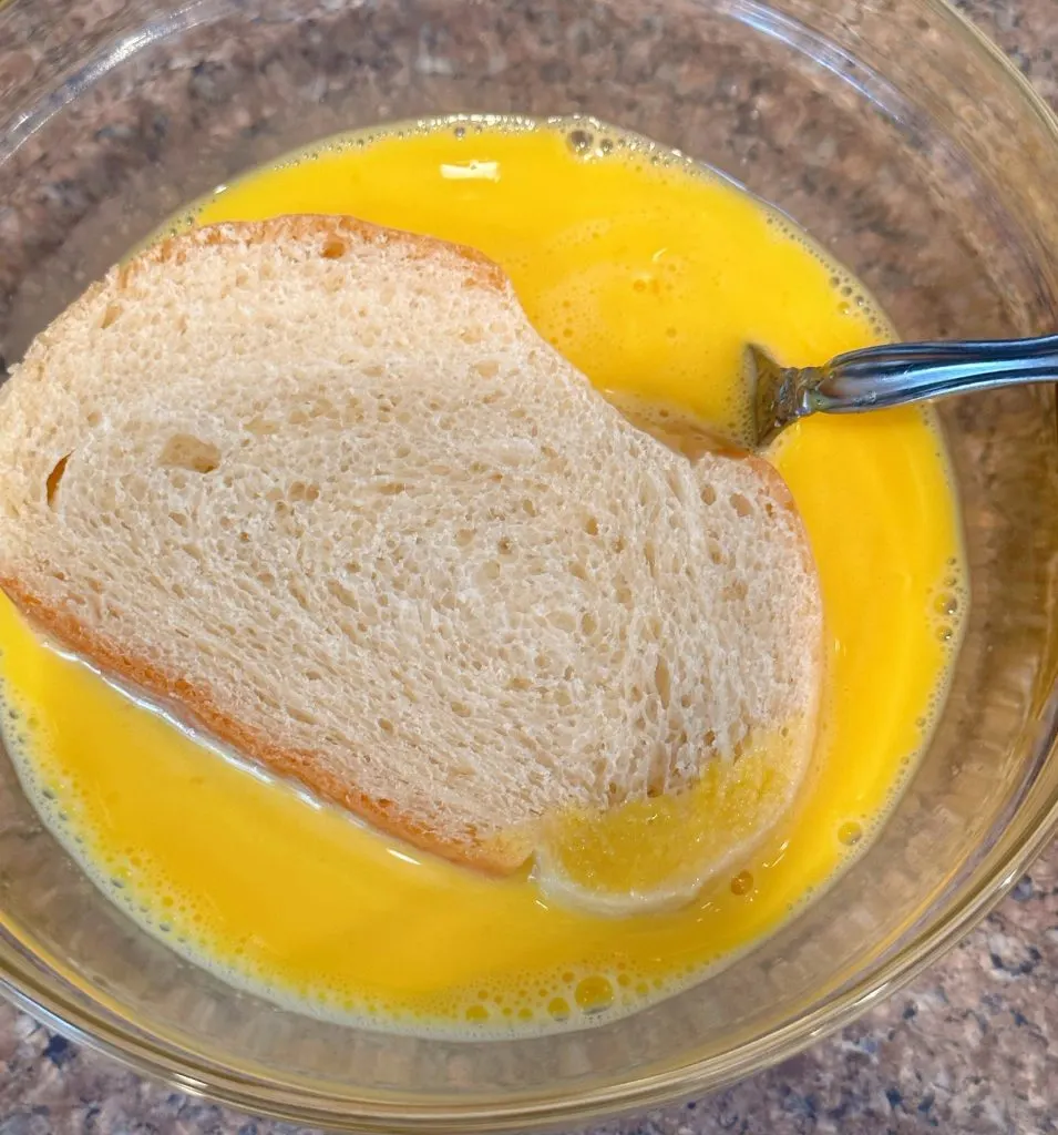 Dipping a slice of bread in the egg batter.