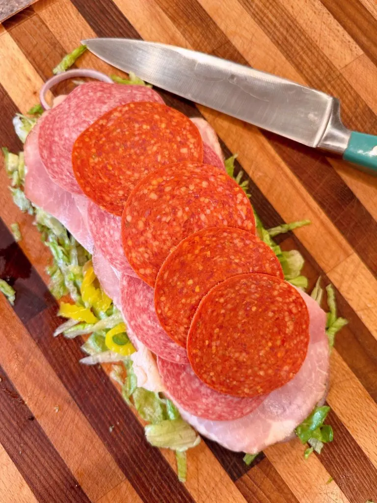 Adding meat and cheese to vegetables of Italian Grinder.