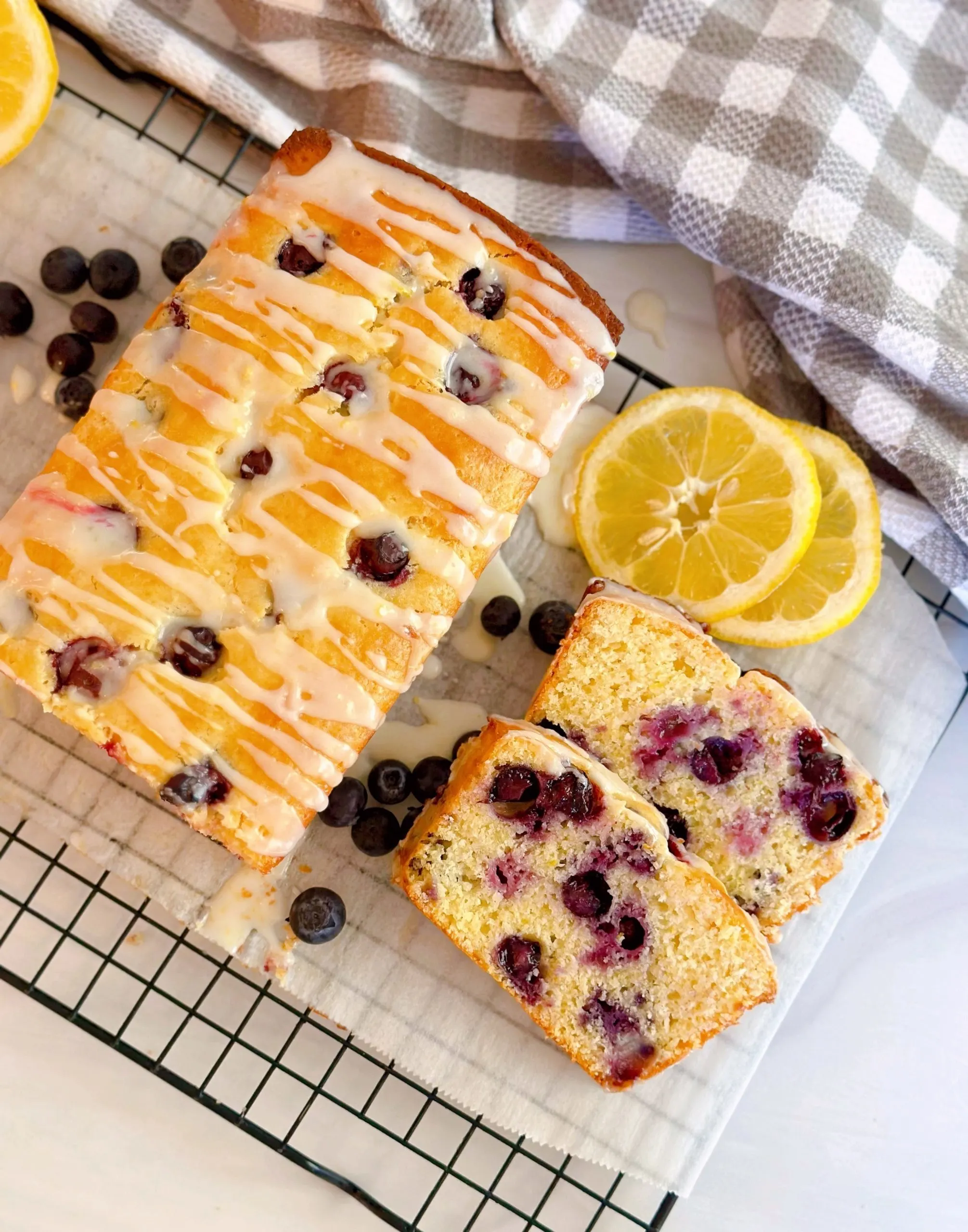 Lemon Blueberry Glazed Bread on a cooling rack with parchment paper and fresh blueberries. Sliced.