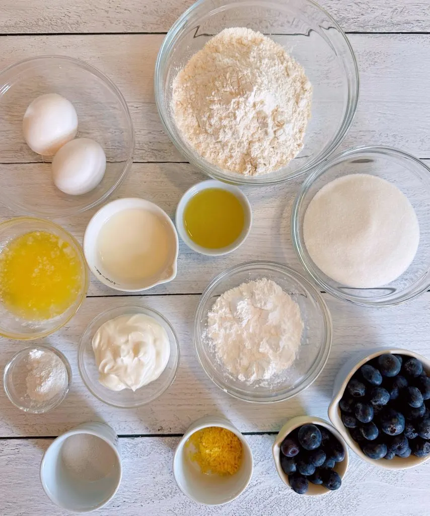 Ingredients for Lemon Blueberry Bread measured out, in bowls, on a white counter.