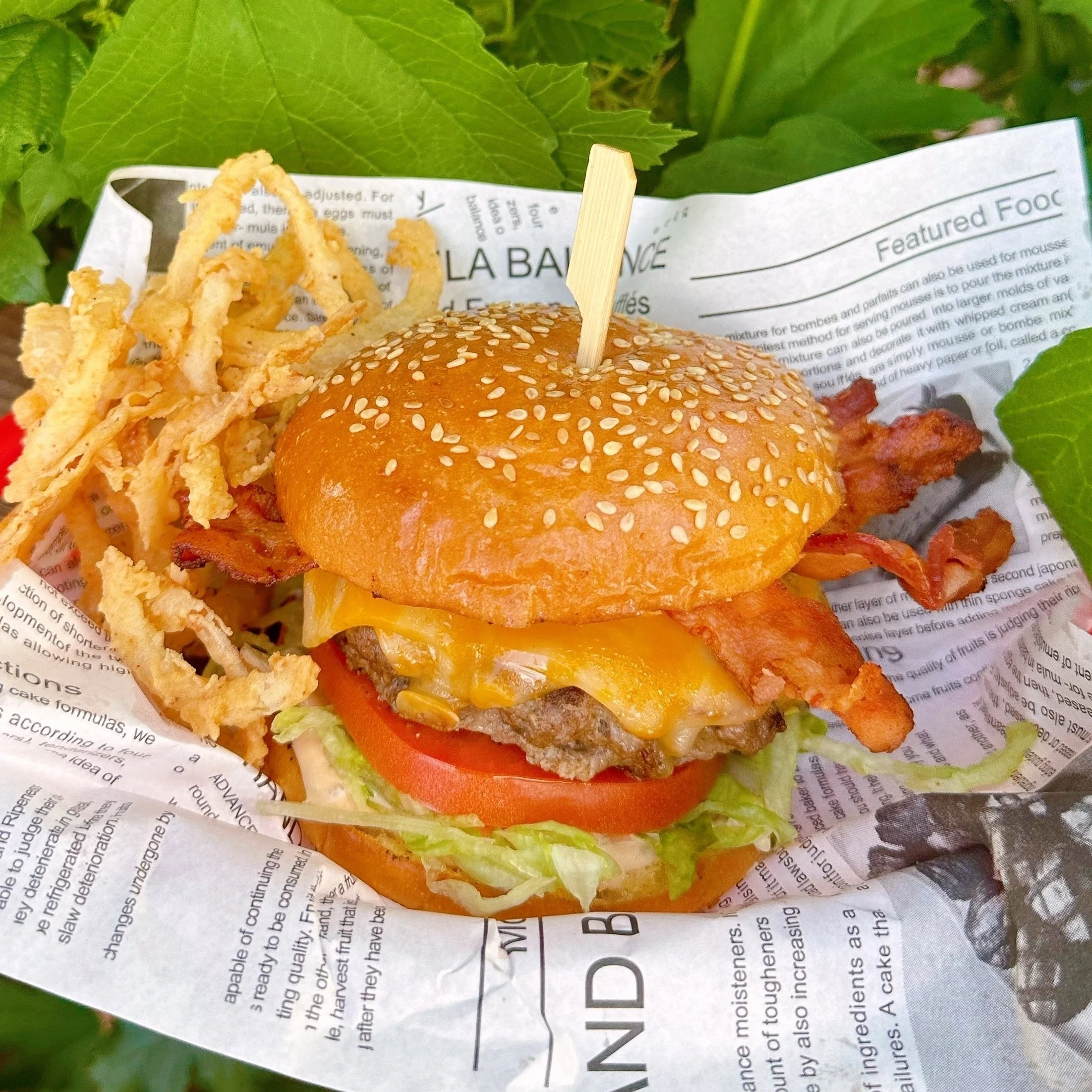 Ultimate Bacon Onion Smash Burgers with cheese in a basket on a parchment printed paper with onion straws on the side.