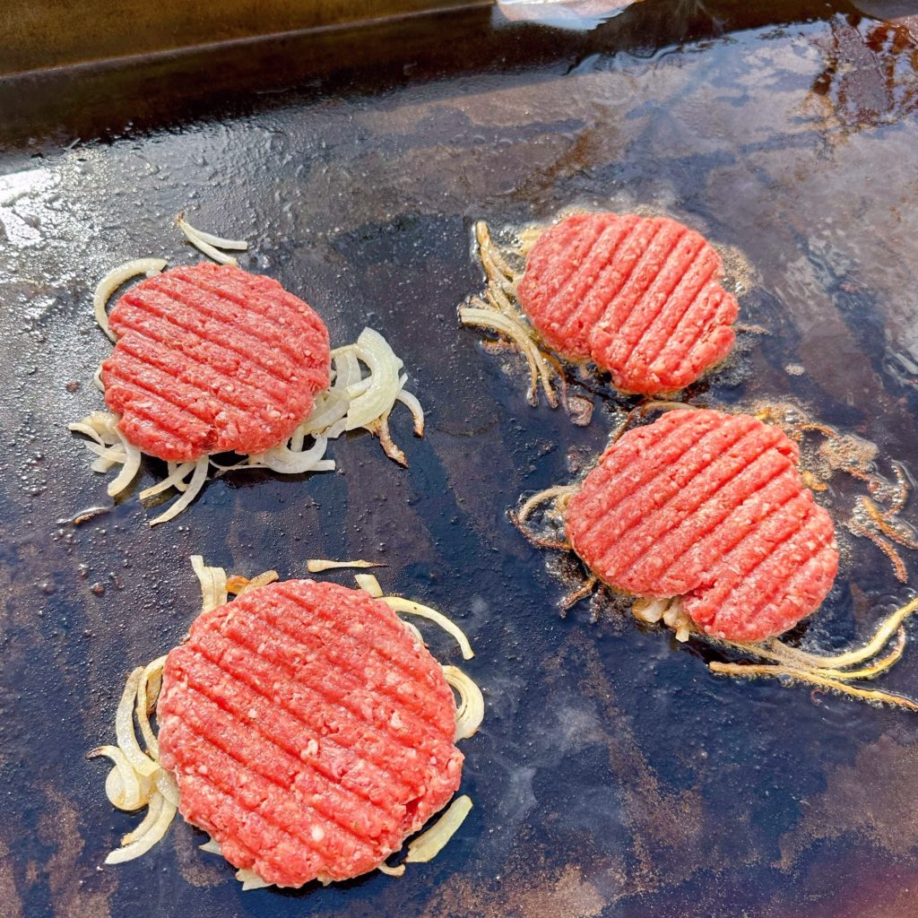 Smashed burgers on hot griddle cooking.
