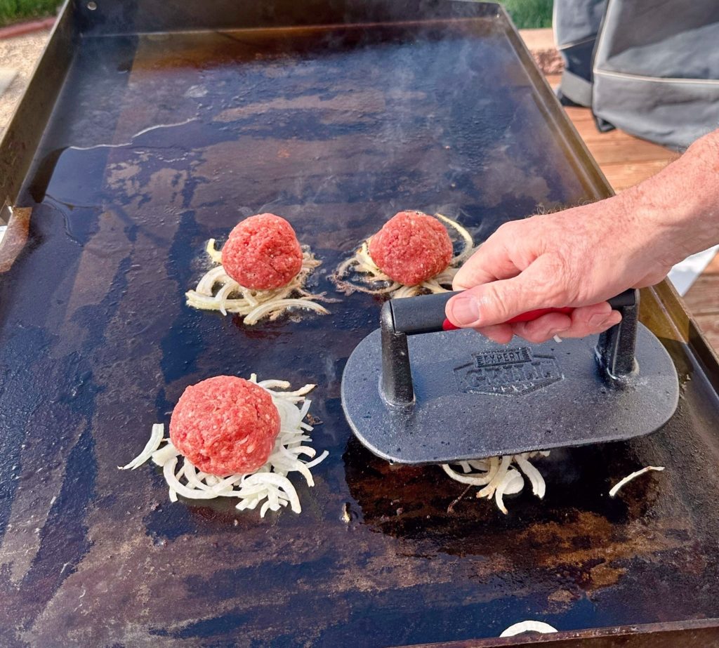 Burger press pressing down on top of each ground beef ball, smashing them.