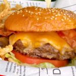 Ultimate Bacon Smash Cheeseburger in a red basket with onion straws.