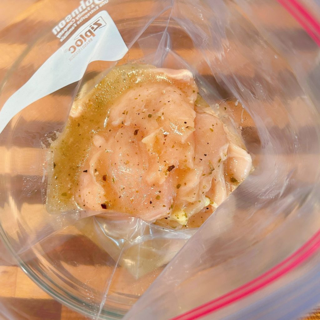 Chicken breast with marinade in a Ziploc bag.