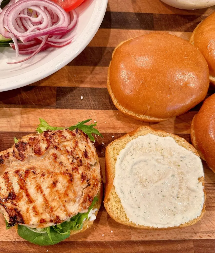 Assembling Chicken Sandwich with buns, chicken, and veggies.