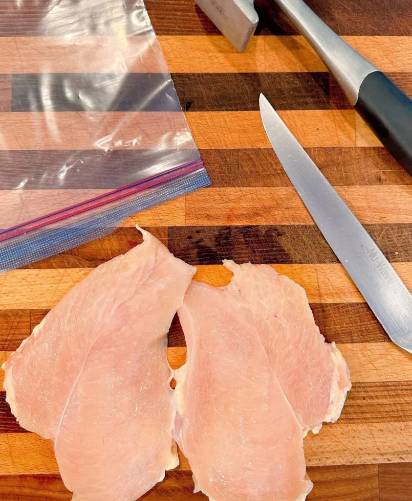 Butterflied Chicken Breast on a cutting board with a knife and plastic bag for tenderizing.