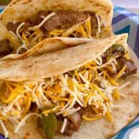 Blackstone Grilled Steak Fajitas on a paper plate with cheese in a flour tortilla.