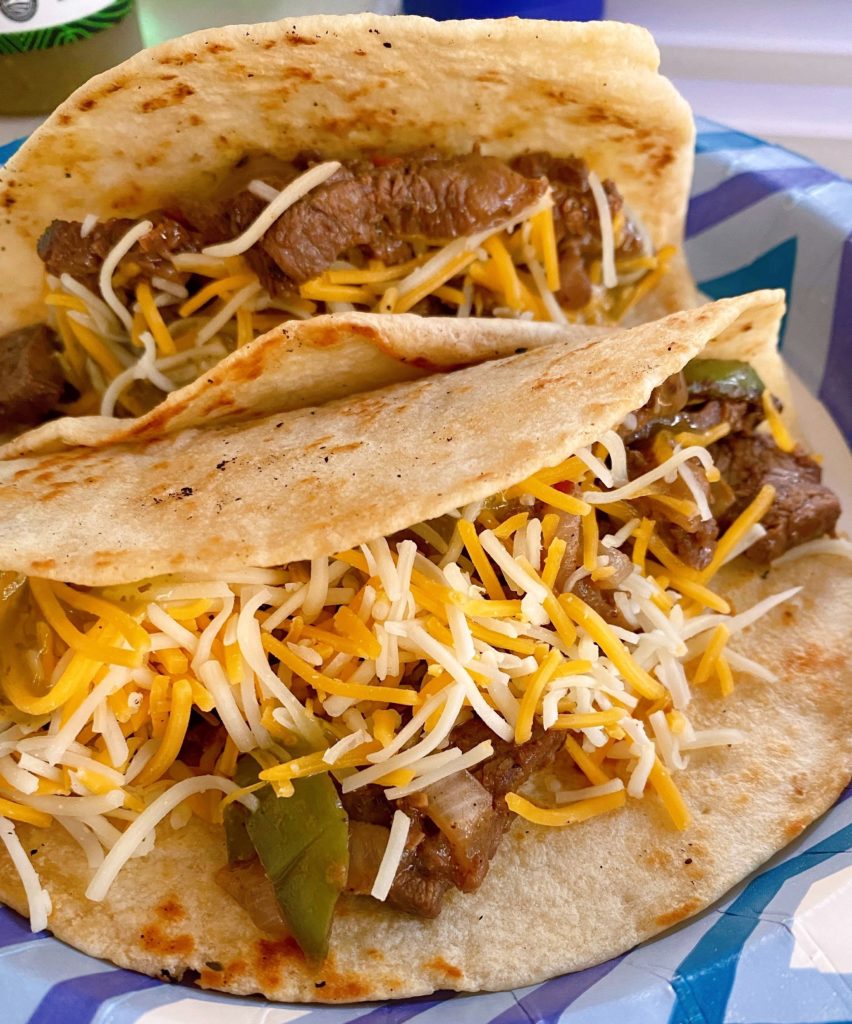 Blackstone Grilled Steak Fajitas on a paper plate with cheese in a flour tortilla.