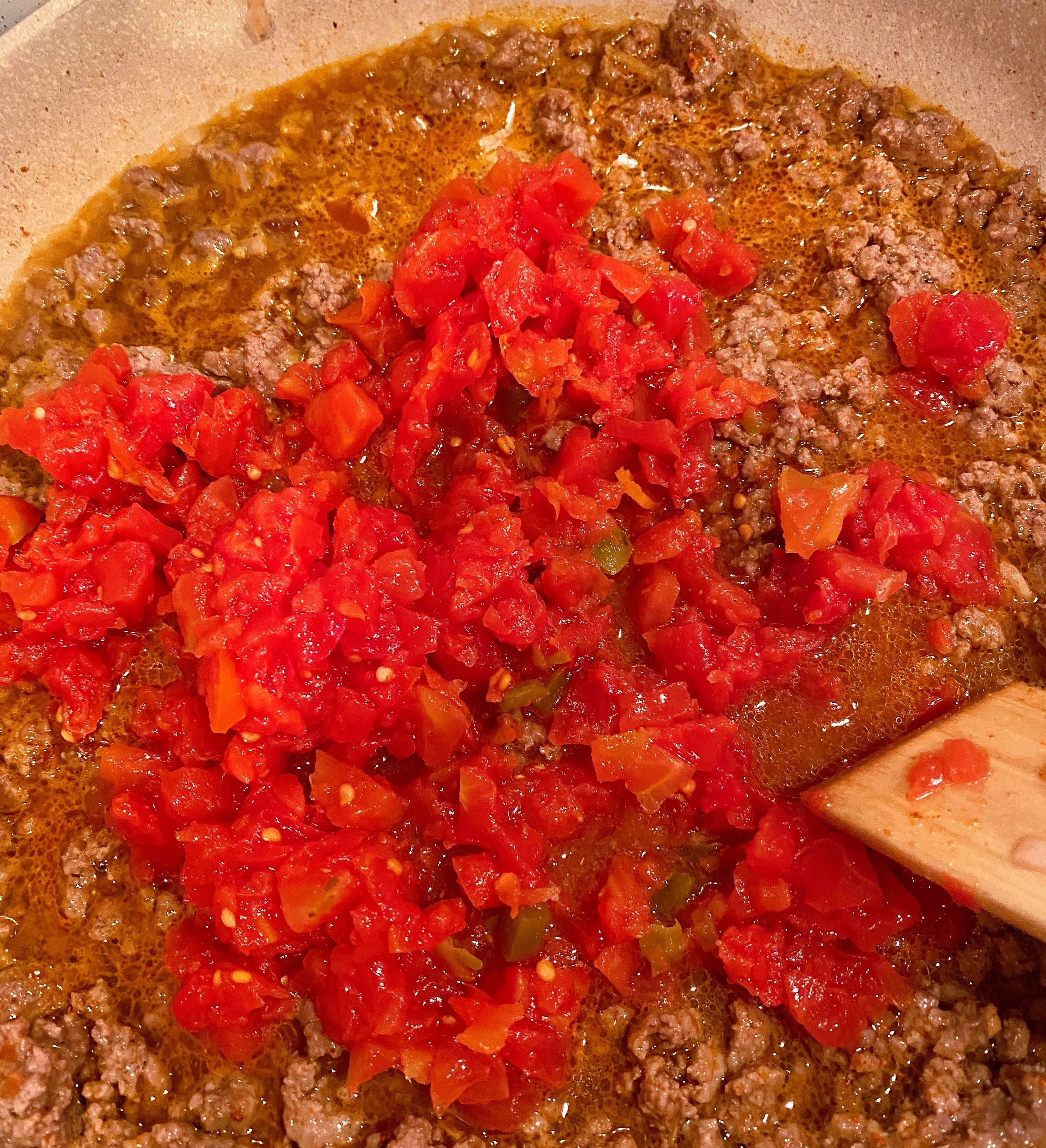 Adding petite diced tomatoes to ground beef.