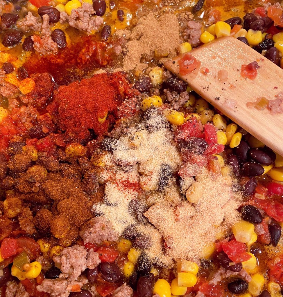 Adding seasonings, beans, corn, and tomato paste.