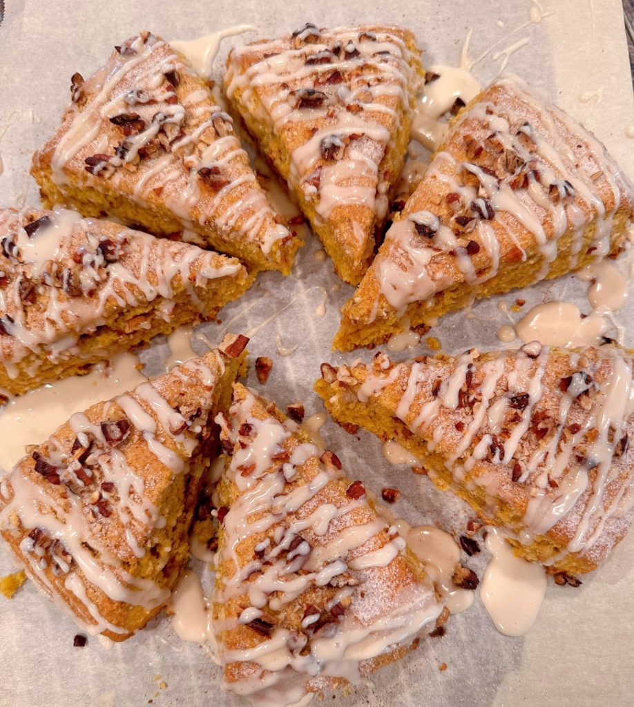 Scones on parchment paper with glaze drizzled over the top of each one.