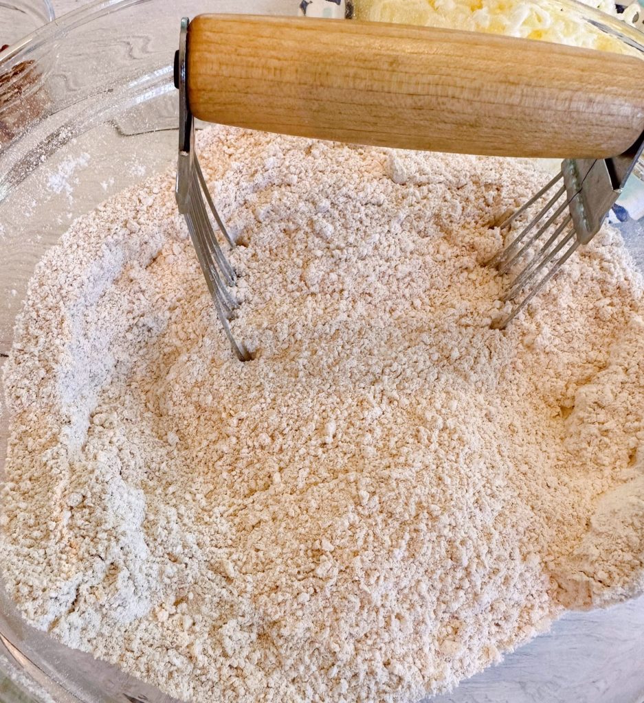 Dry ingredients combined in a glass bowl with a pastry blender.