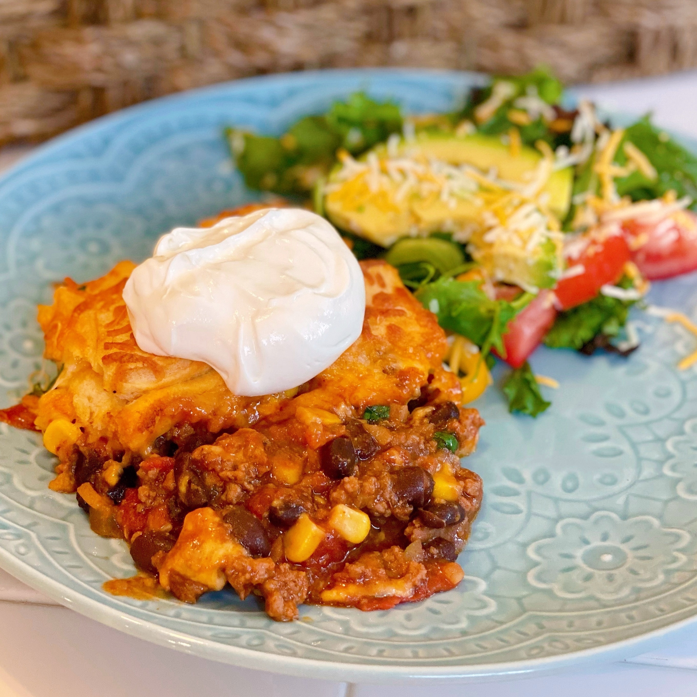 Cornbread Chili Taco Casserole on a dinner plate topped with sour cream and served with a side salad.