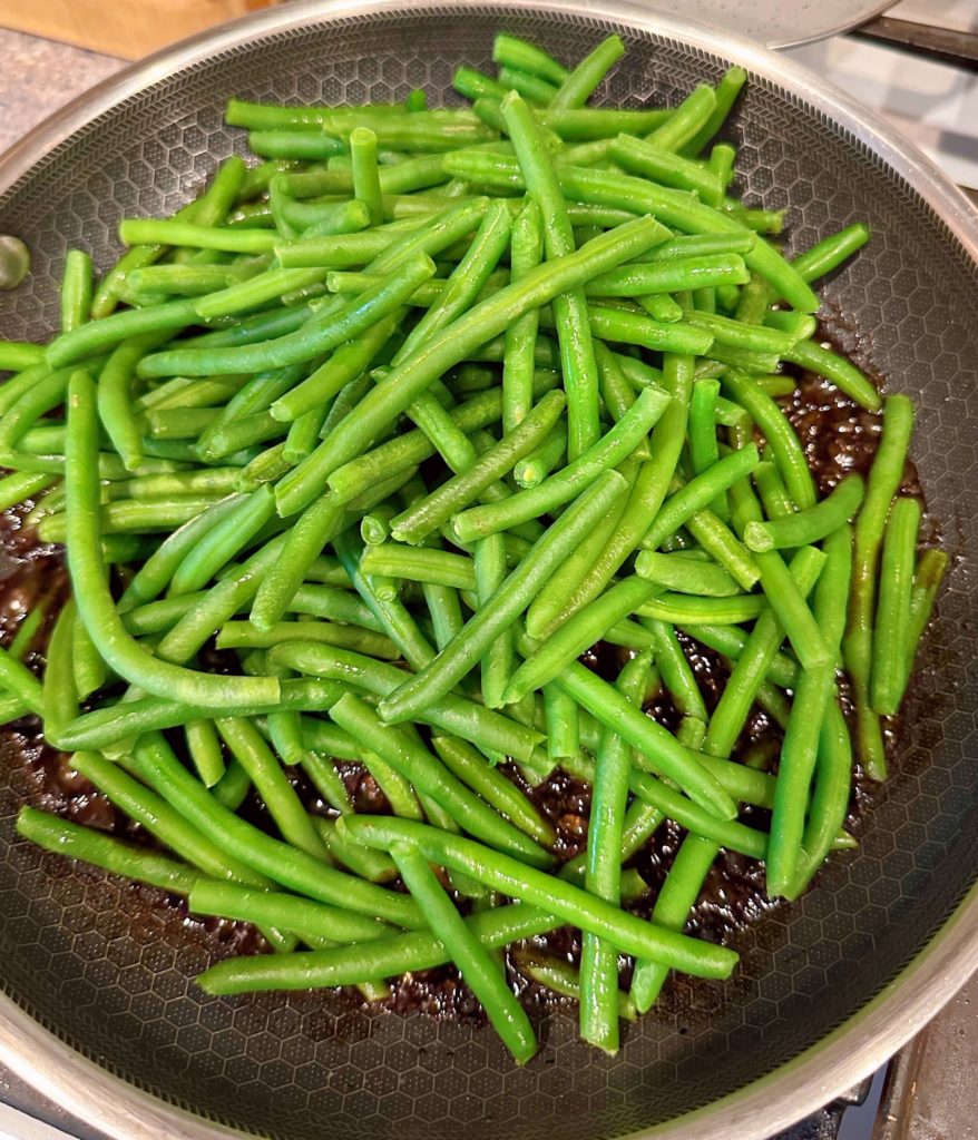 Adding Green Beans to Balsamic Glaze in large skillet on stove top.
