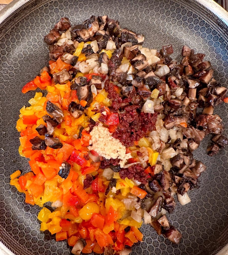 Vegetables, garlic, and minced sun-dried tomatoes in a large skillet on stove top.