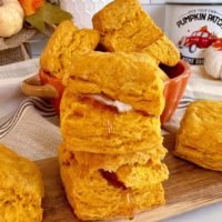 Pumpkin Biscuits stacked on a cutting board, stacked, with honey and butter.