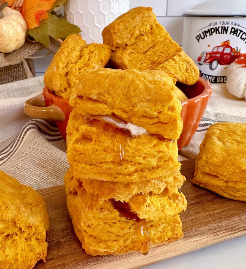 Pumpkin Biscuits stacked on a cutting board, stacked, with honey and butter.