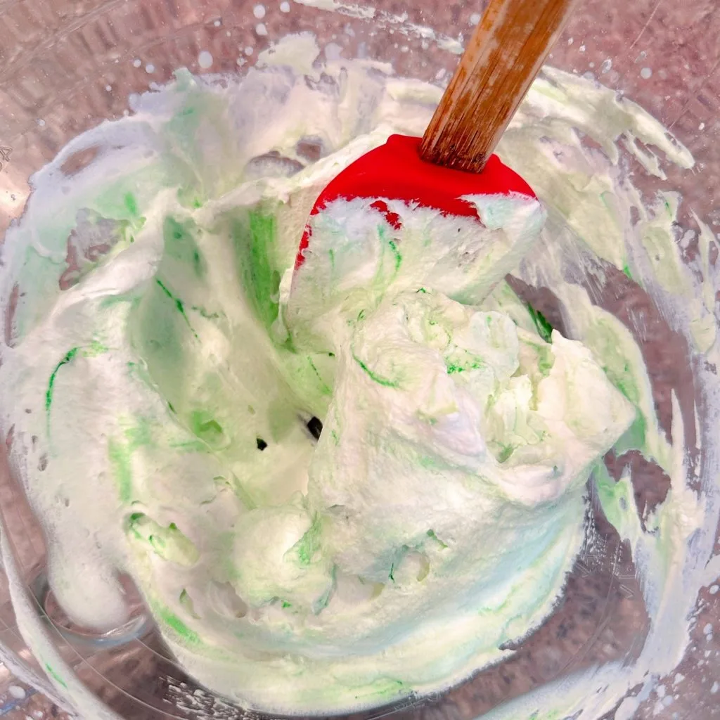 Adding green food coloring to whipped cream frosting.