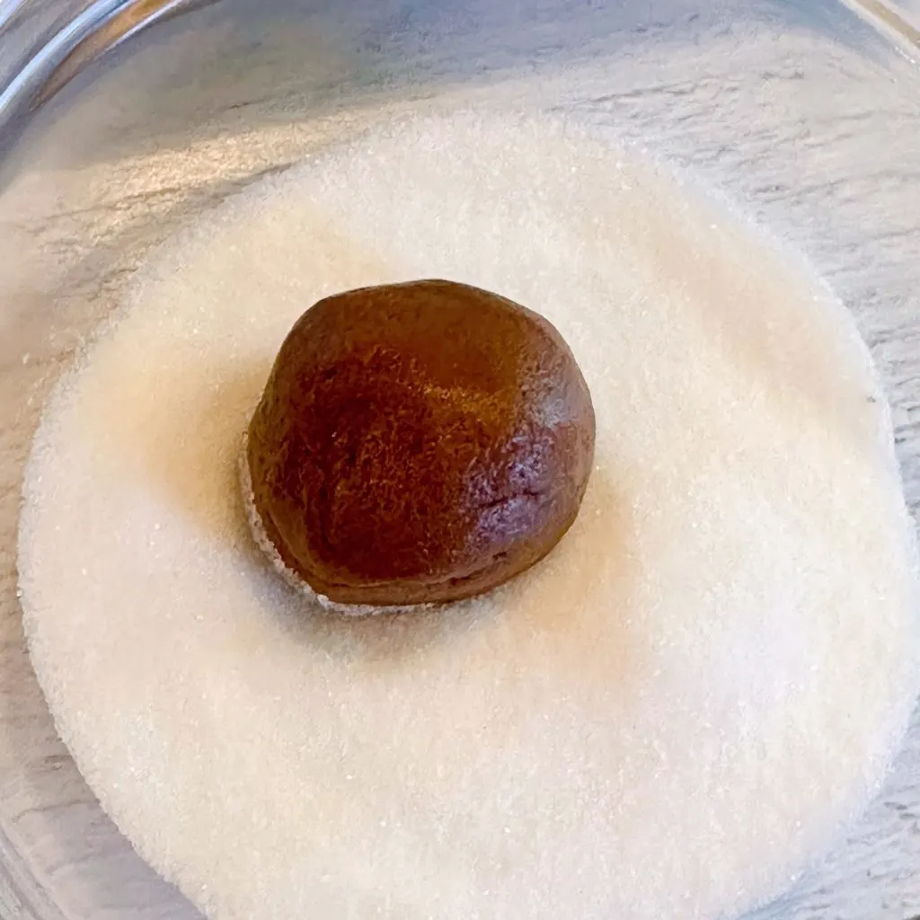 Chocolate cookie dough shaped into a ball and being rolled in granulated sugar.