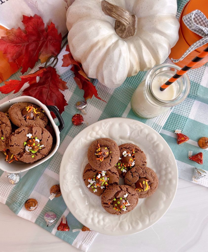 Chocolate Peanut Butter Blossom Cookies with a glass of milk and surrounded by chocolate kisses.