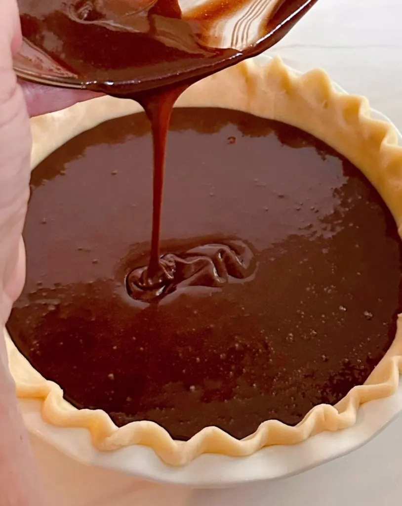 Pouring chocolate pie filling into prepared pie crust.
