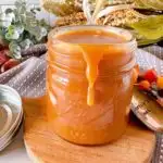 Salted Caramel Sauce in a glass jar on a small wooden cutting board.