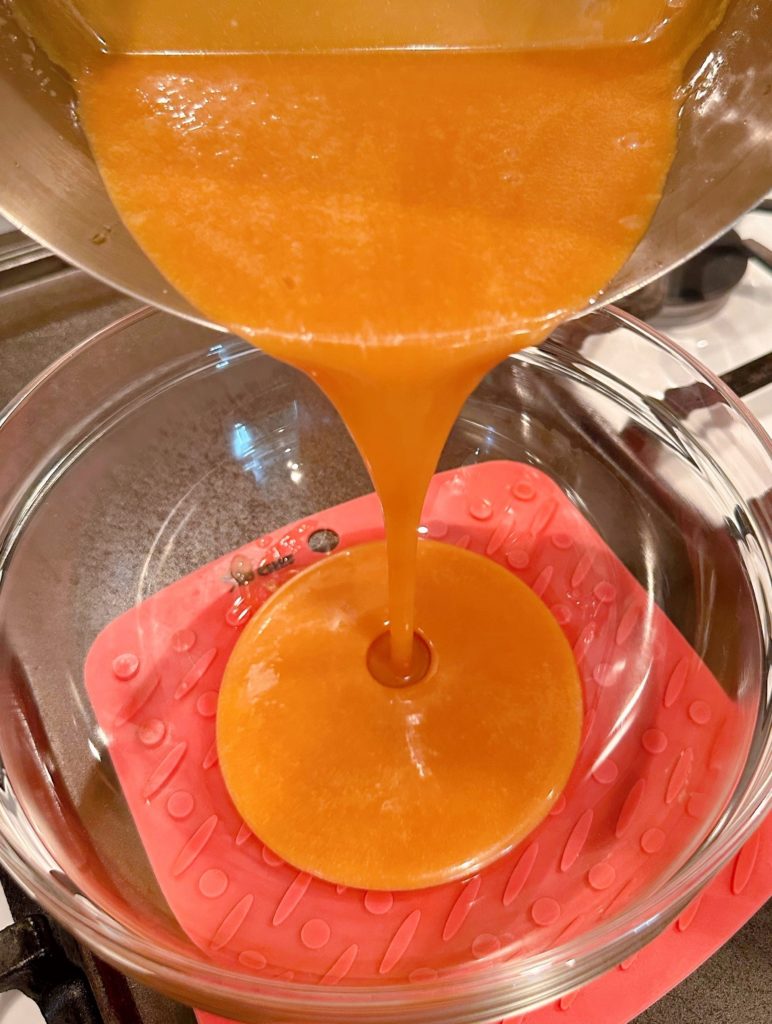 Pouring caramel into a glass bowl to cool.