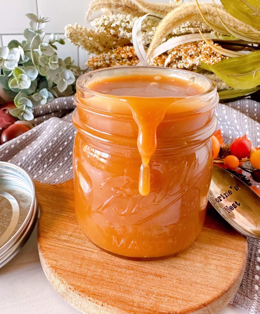 Salted Caramel Sauce in a glass jar on a small wooden cutting board.