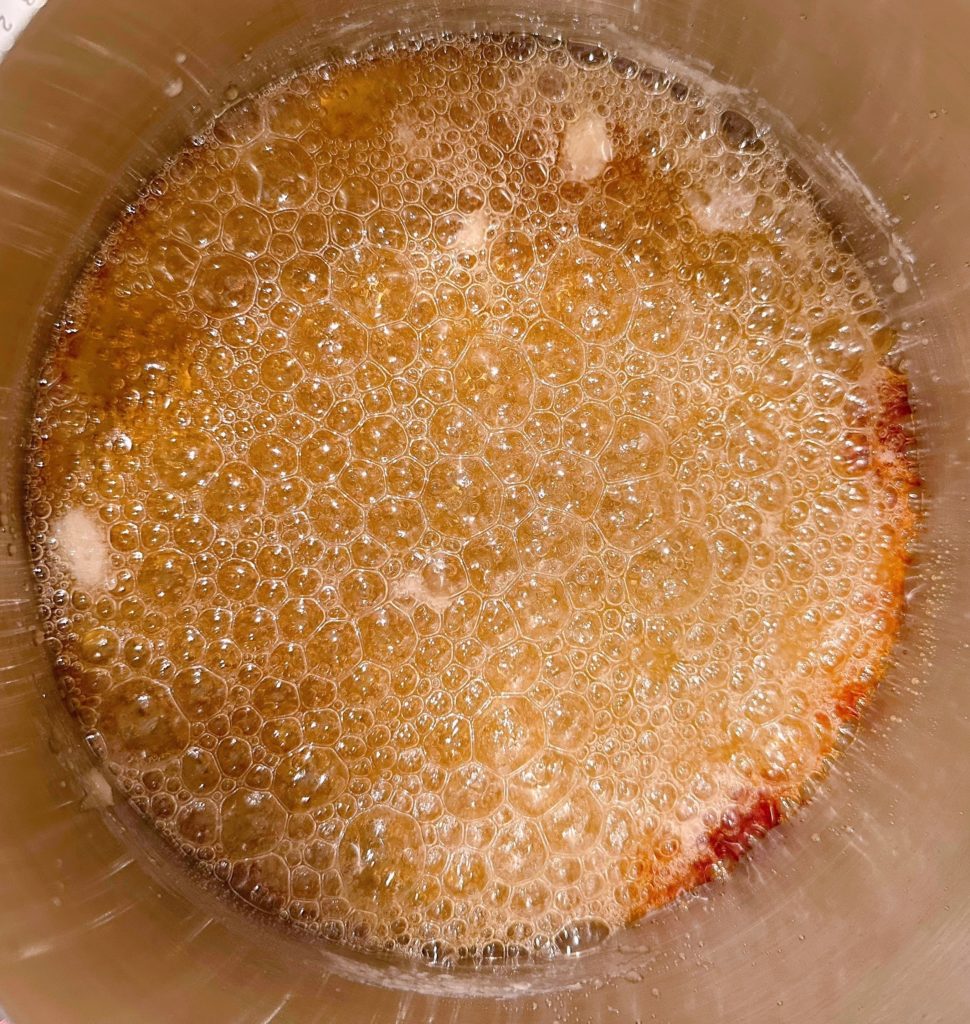 Boiling sugar water turning a reddish orange color in the sauce pan.