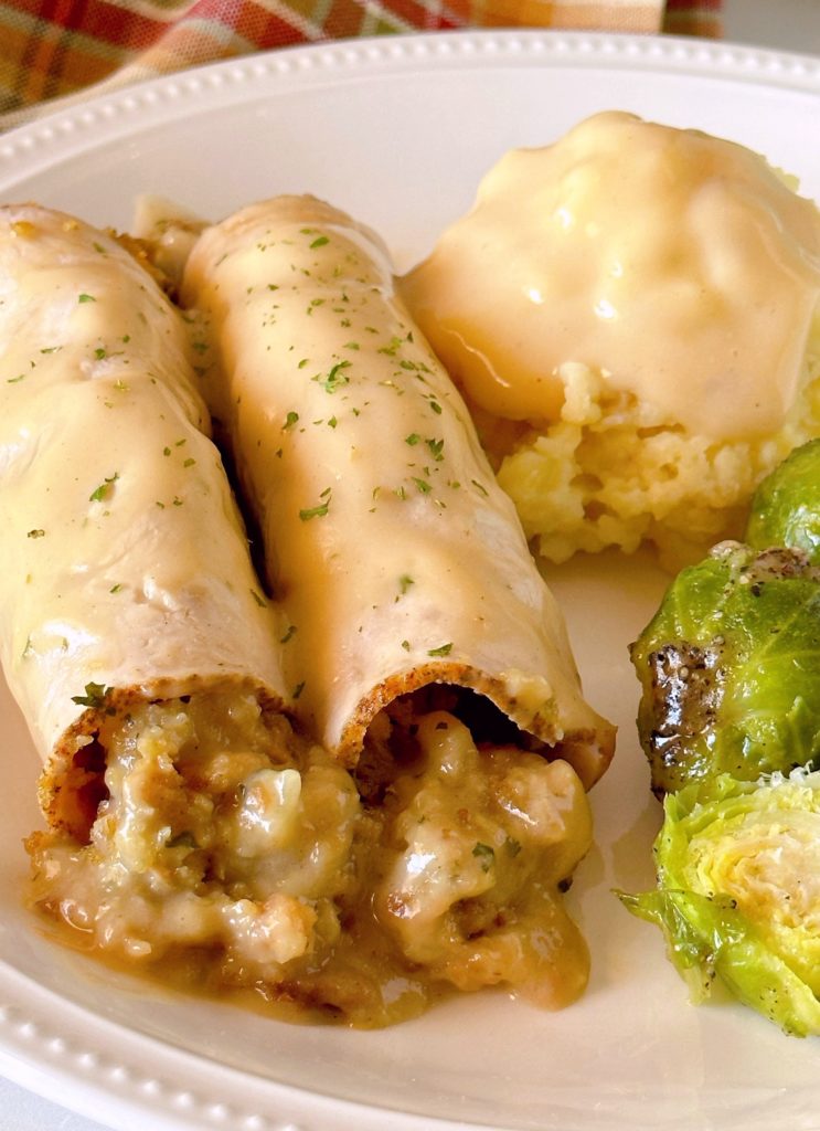 Turkey Roll-ups with stuffing on a dinner plate with mashed potatoes and gravy and a side of Brussels sprouts.