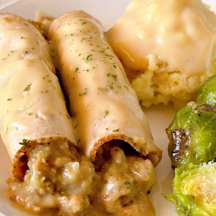 Turkey Roll-ups with stuffing on a dinner plate with mashed potatoes and gravy and a side of Brussels sprouts.