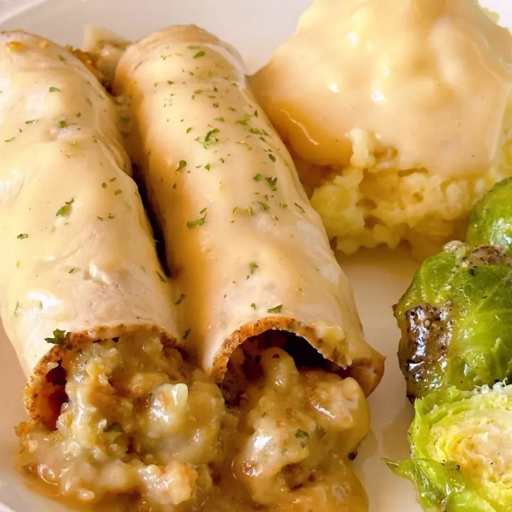 Turkey Roll-ups with stuffing on a dinner plate with mashed potatoes and gravy and a side of Brussels sprouts.