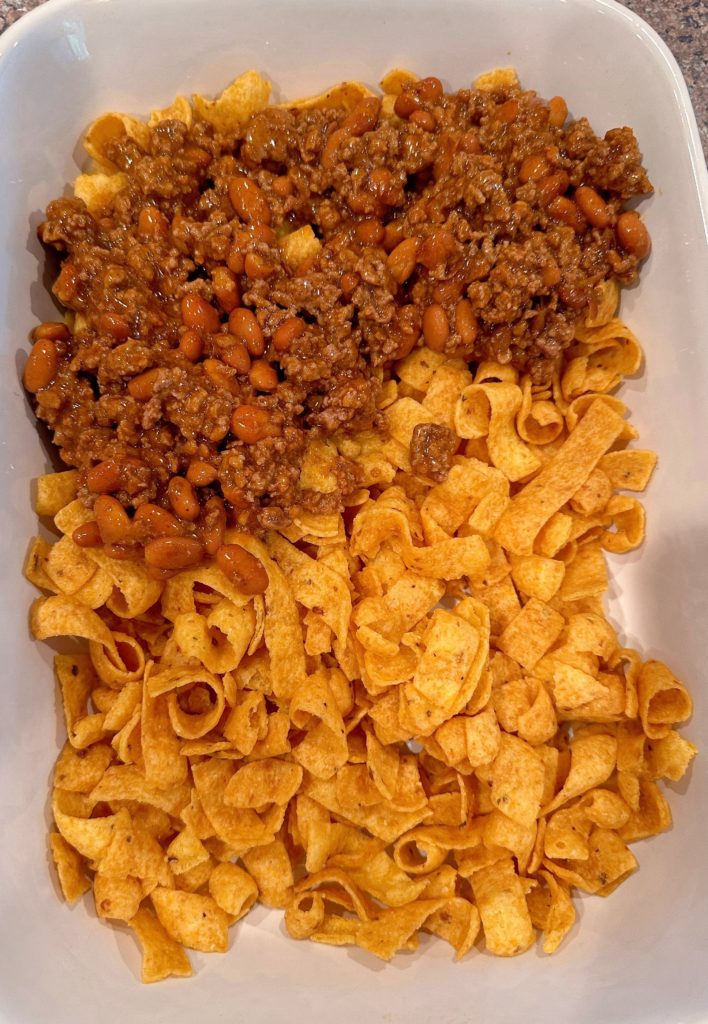 Evenly spreading meat mixture over frito corn chips.