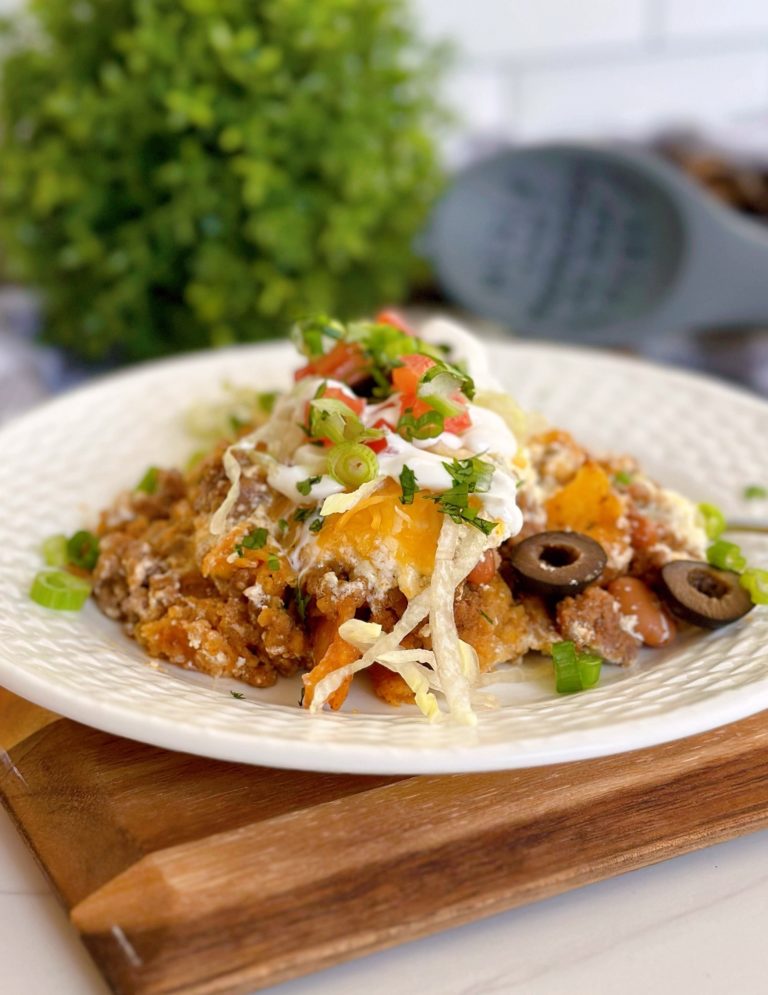 Serving of Walking taco casserole on a white plate with taco toppings.