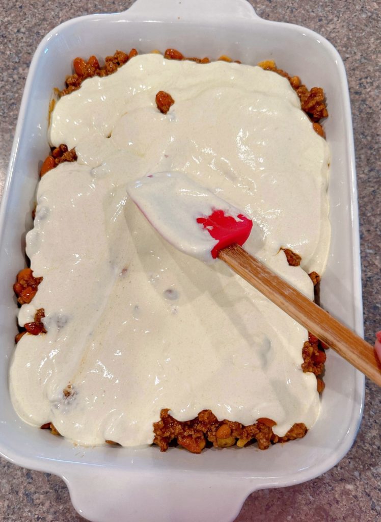 Spreading green enchilada sauce and sour cream over the top of the meat mixture.