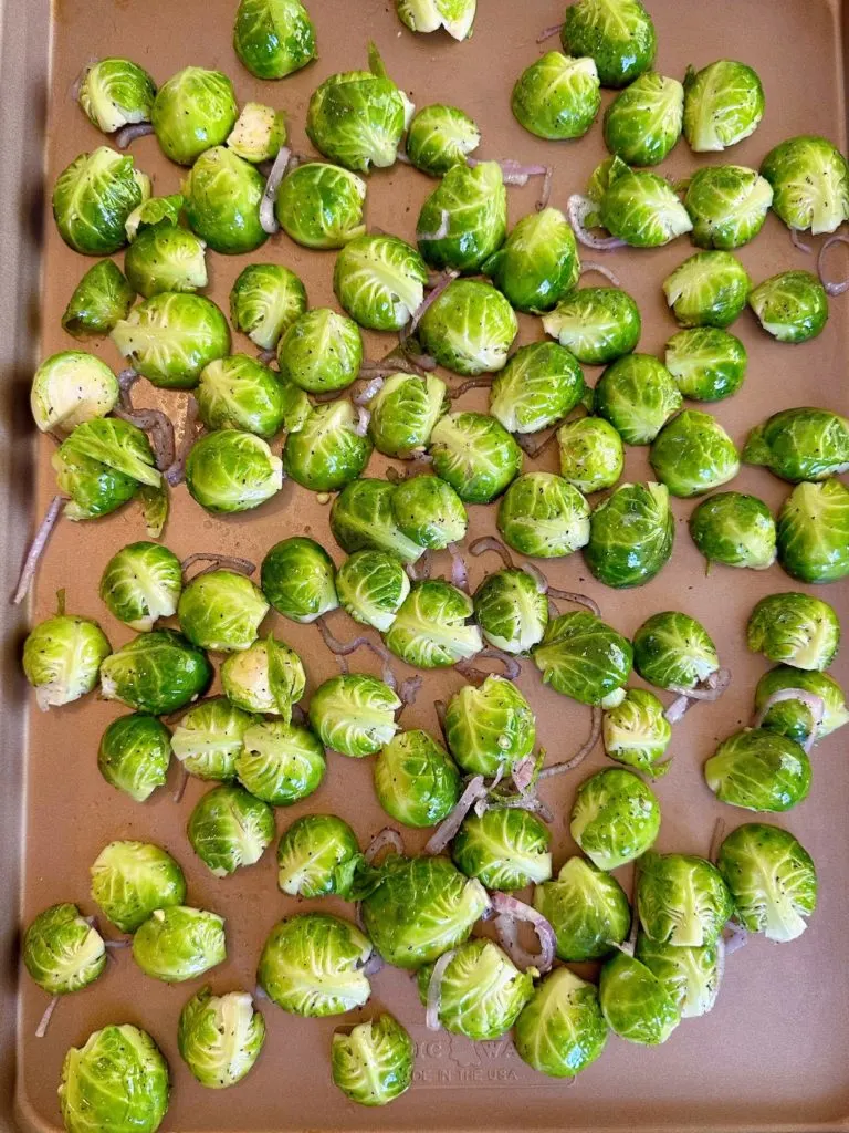 Baking sheet with cut and trimmed Brussels sprouts and shallots.