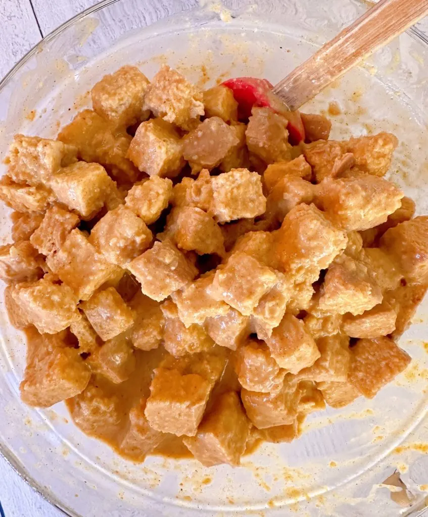 Bread cubes coated with pumpkin custard mixture in a large mixing bowl.