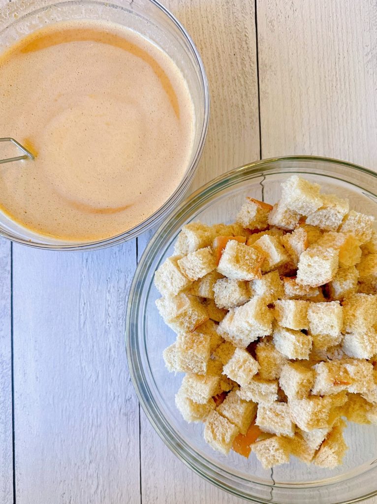 Bread cubes in a large mixing bowl with egg mixture next to it.