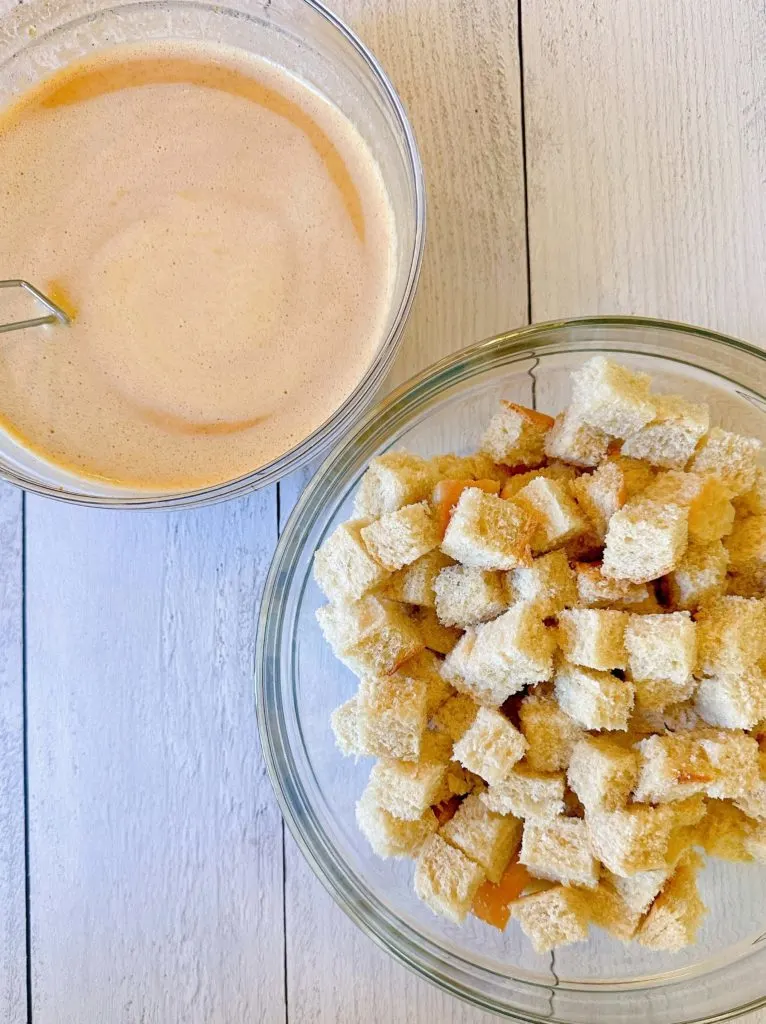 Bread cubes in a large mixing bowl with egg mixture next to it.