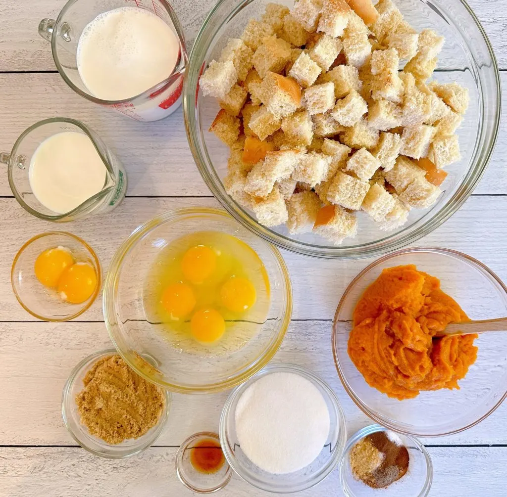 Ingredients in bowls on a white board for Pumpkin Pecan Bread Pudding.