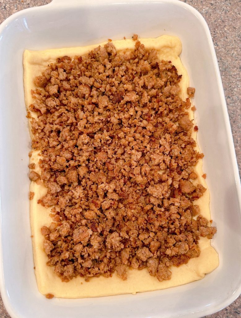 Sprinkled breakfast sausage over crescent roll dough in baking dish.