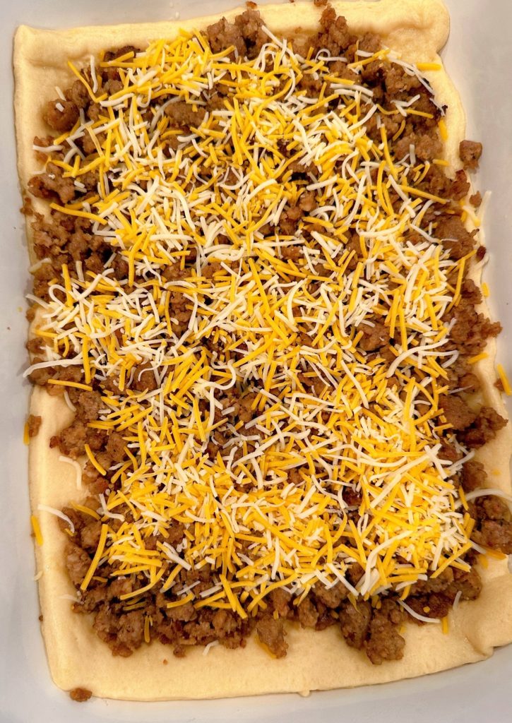 Cheese sprinkled over sausage in the baking dish.