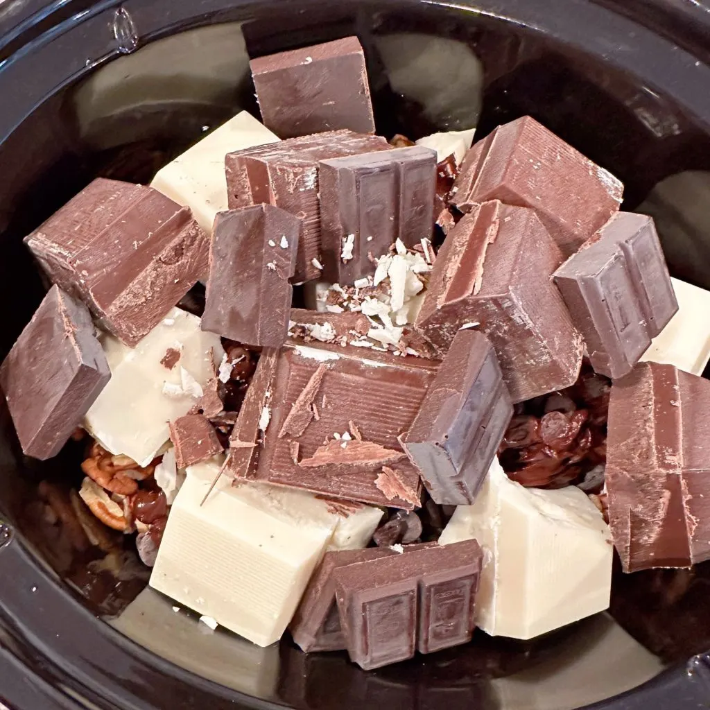 Chocolates are layered on top of pecans in the slow cooker.