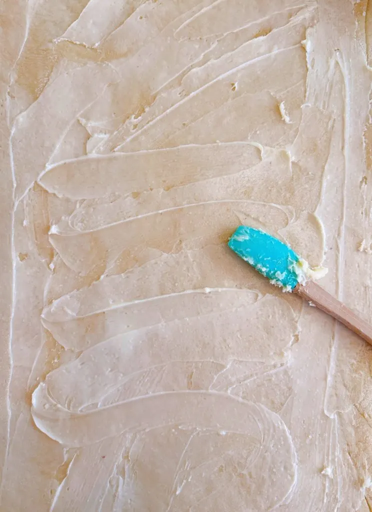 Spreading soften butter on rolled bread dough.