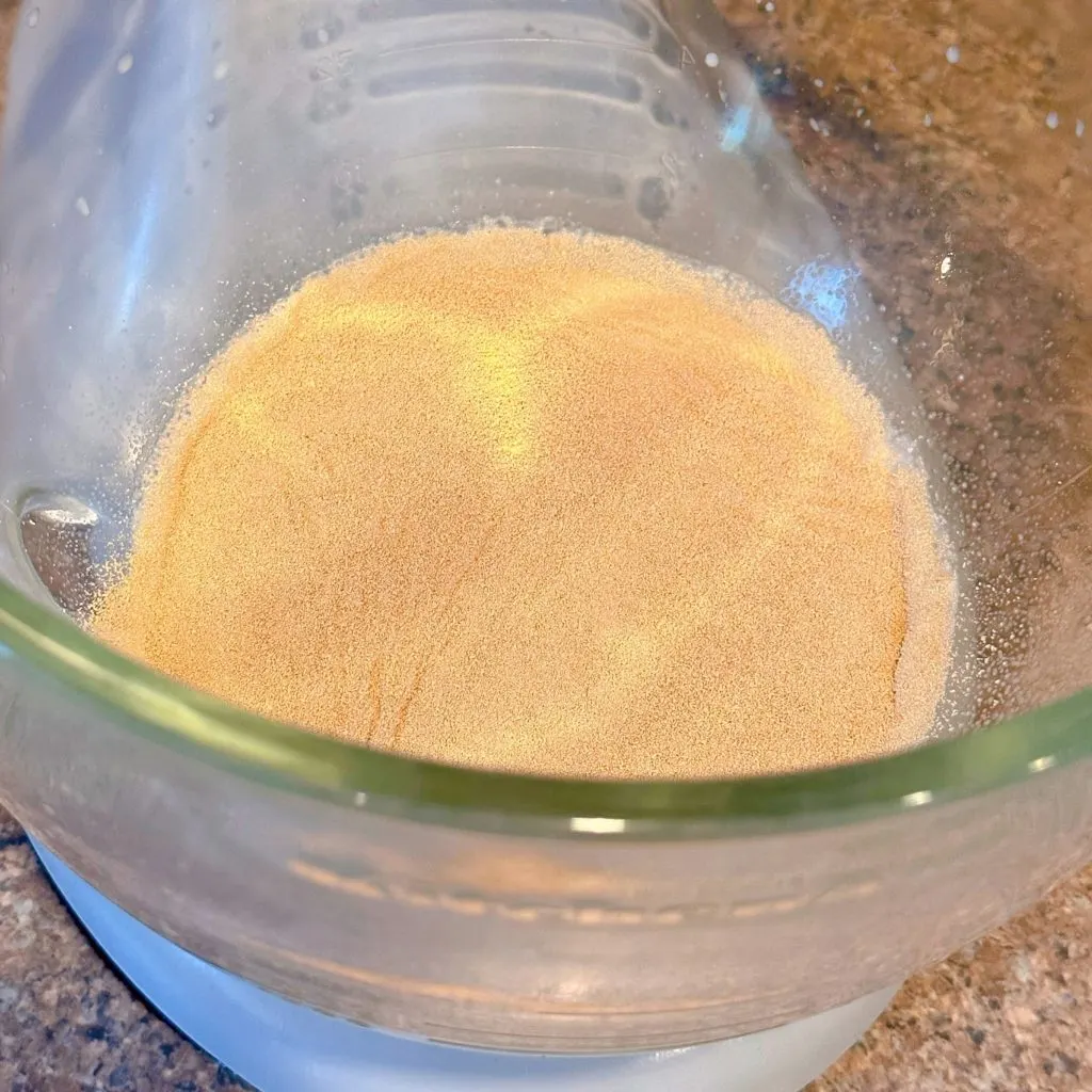 Yeast is sprinkled on top of the warm milk in the bowl of mixer.