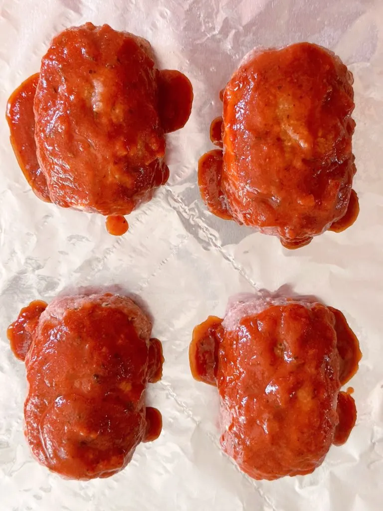 Each mini meatloaf is covered in pasta sauce on the baking sheet.