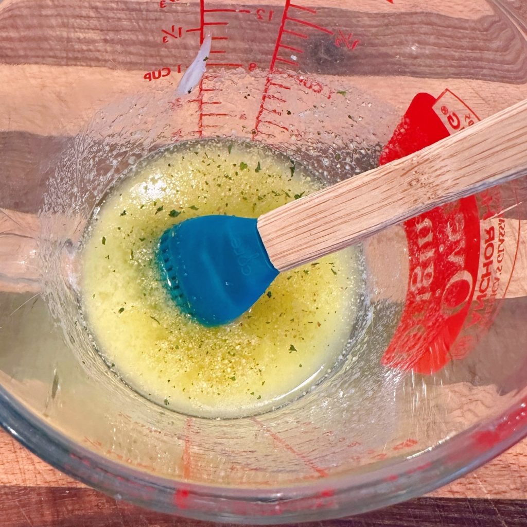 Melted garlic butter in a glass measuring cup with pastry brush.