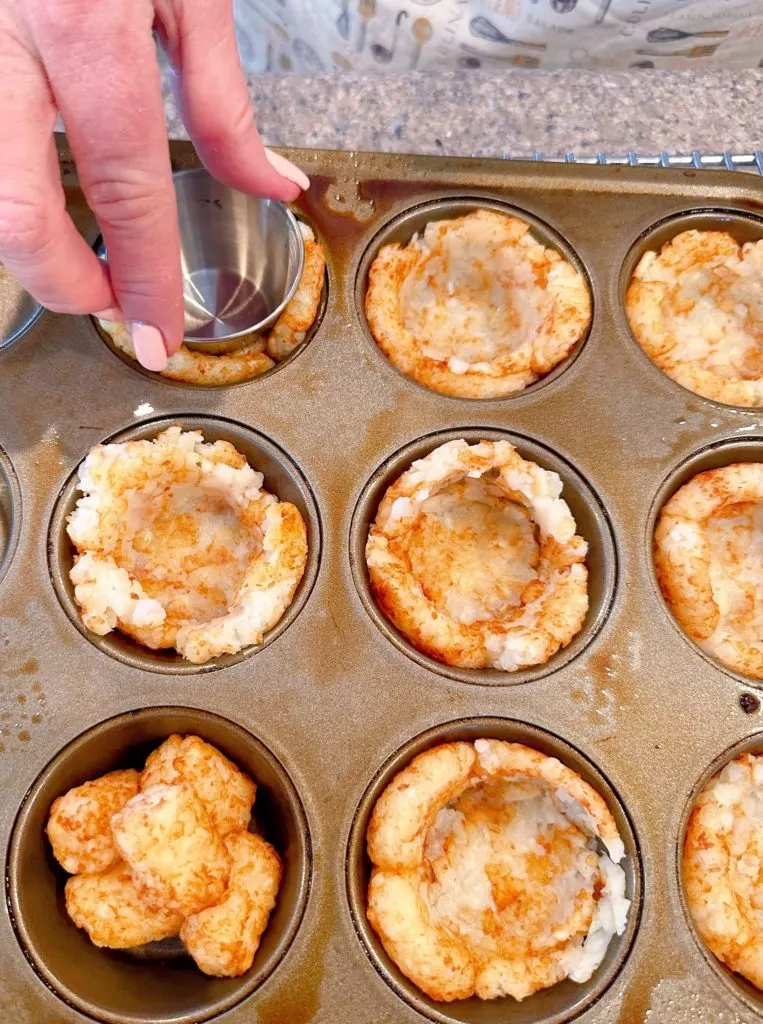 Using a small metal butter dipping cup to press down the partially baked tater tots to create a cup.